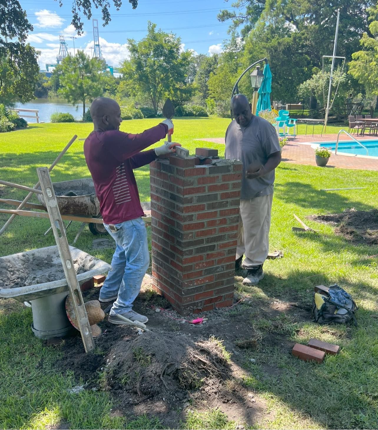 Two men are working on a brick chimney in a backyard.