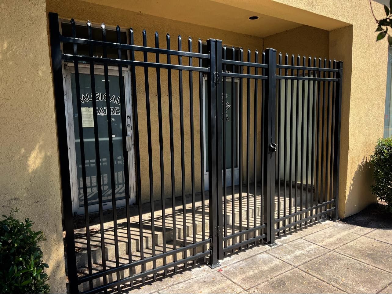 A black wrought iron fence surrounds a building with a green door.