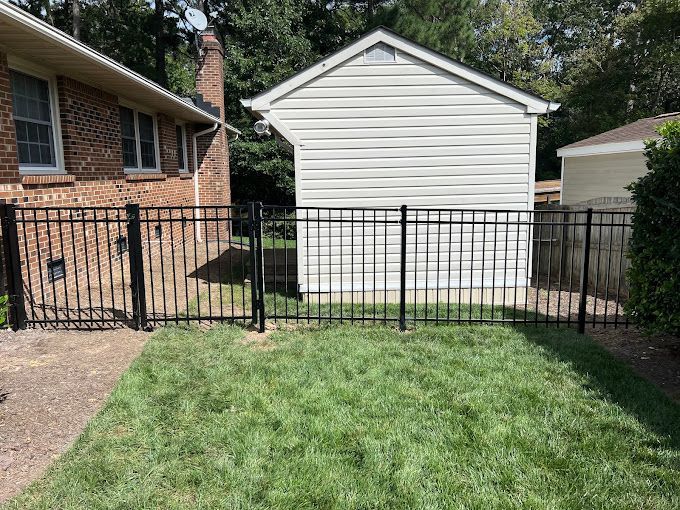 A black fence surrounds a lush green yard in front of a white house.