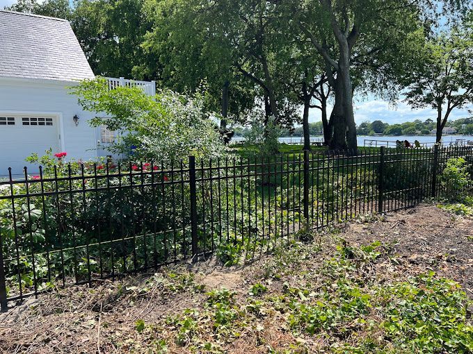 A black fence surrounds a yard with a white house in the background.