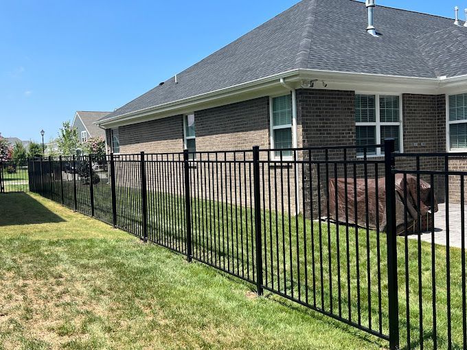 A black metal fence is in front of a brick house.