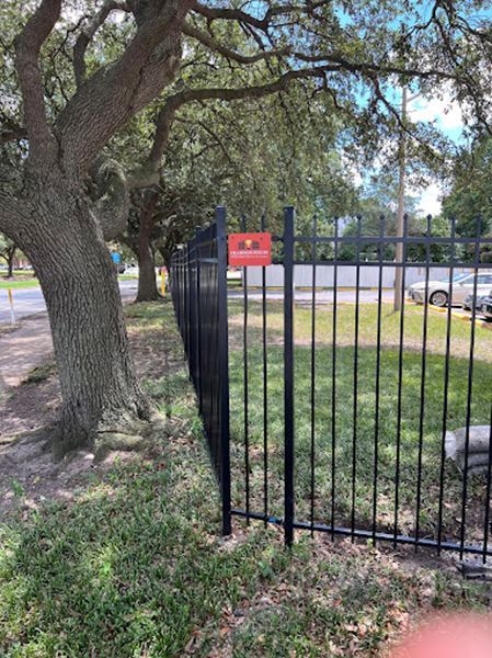 A black metal fence is surrounded by grass and trees in a park.