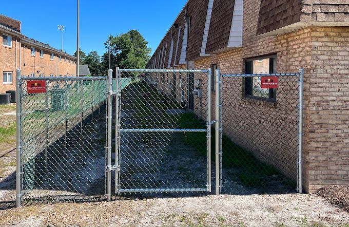 A chain link fence with a gate in front of a brick building.