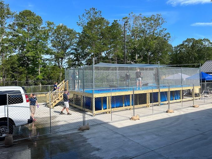 A large swimming pool is being built in a parking lot behind a chain link fence.
