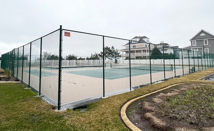 A tennis court behind a chain link fence with houses in the background.
