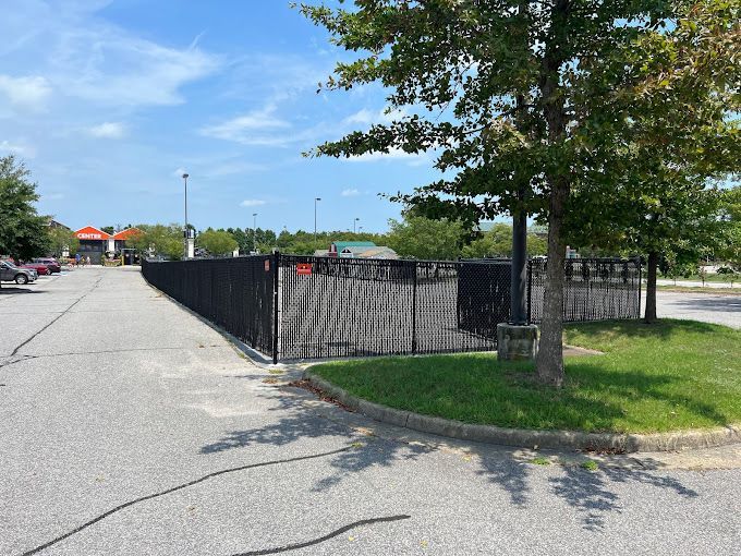 A black fence surrounds a parking lot with a tree in the foreground.