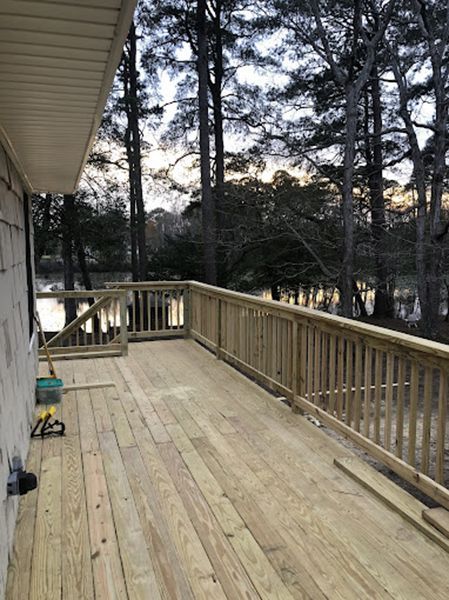 A wooden deck with a railing overlooking a lake surrounded by trees.