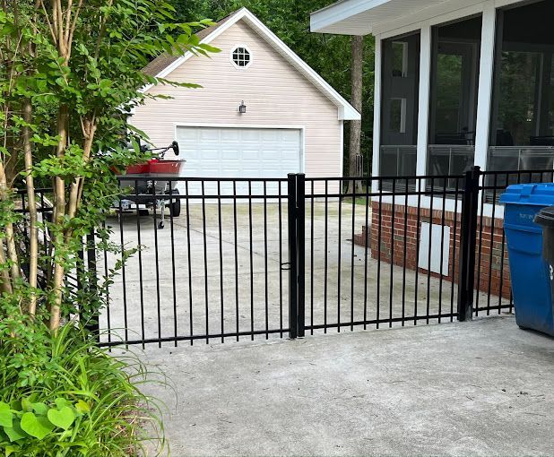 A black metal fence surrounds a driveway in front of a house.