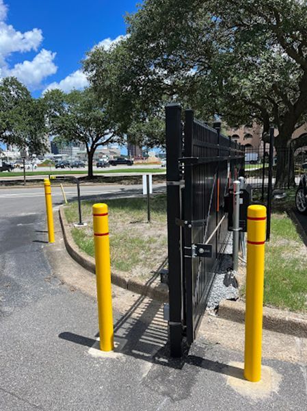 A black gate is surrounded by yellow poles on the side of the road.