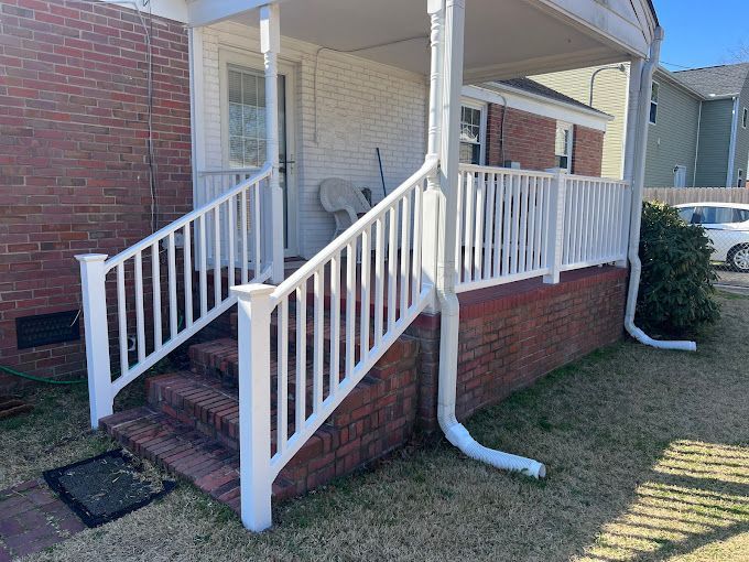 There is a white railing on the porch of a brick house.