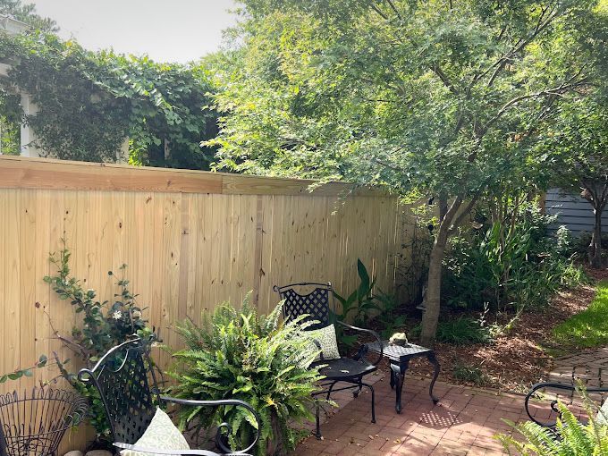 A wooden fence surrounds a patio area with chairs and a table.