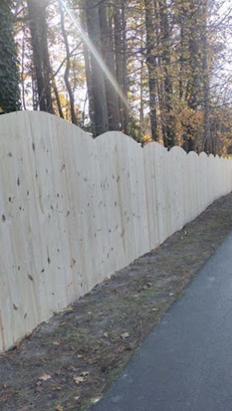 A wooden fence is along the side of a road in the woods.