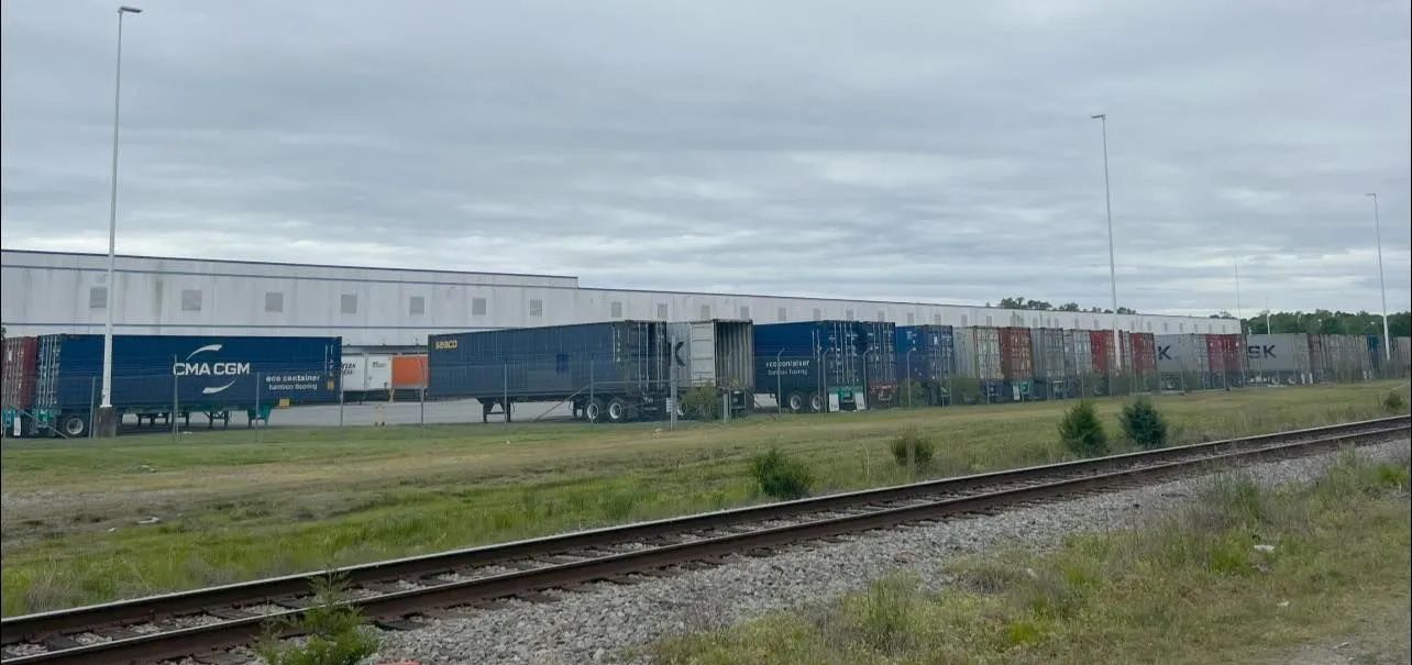 A train is going down the tracks in front of a warehouse.