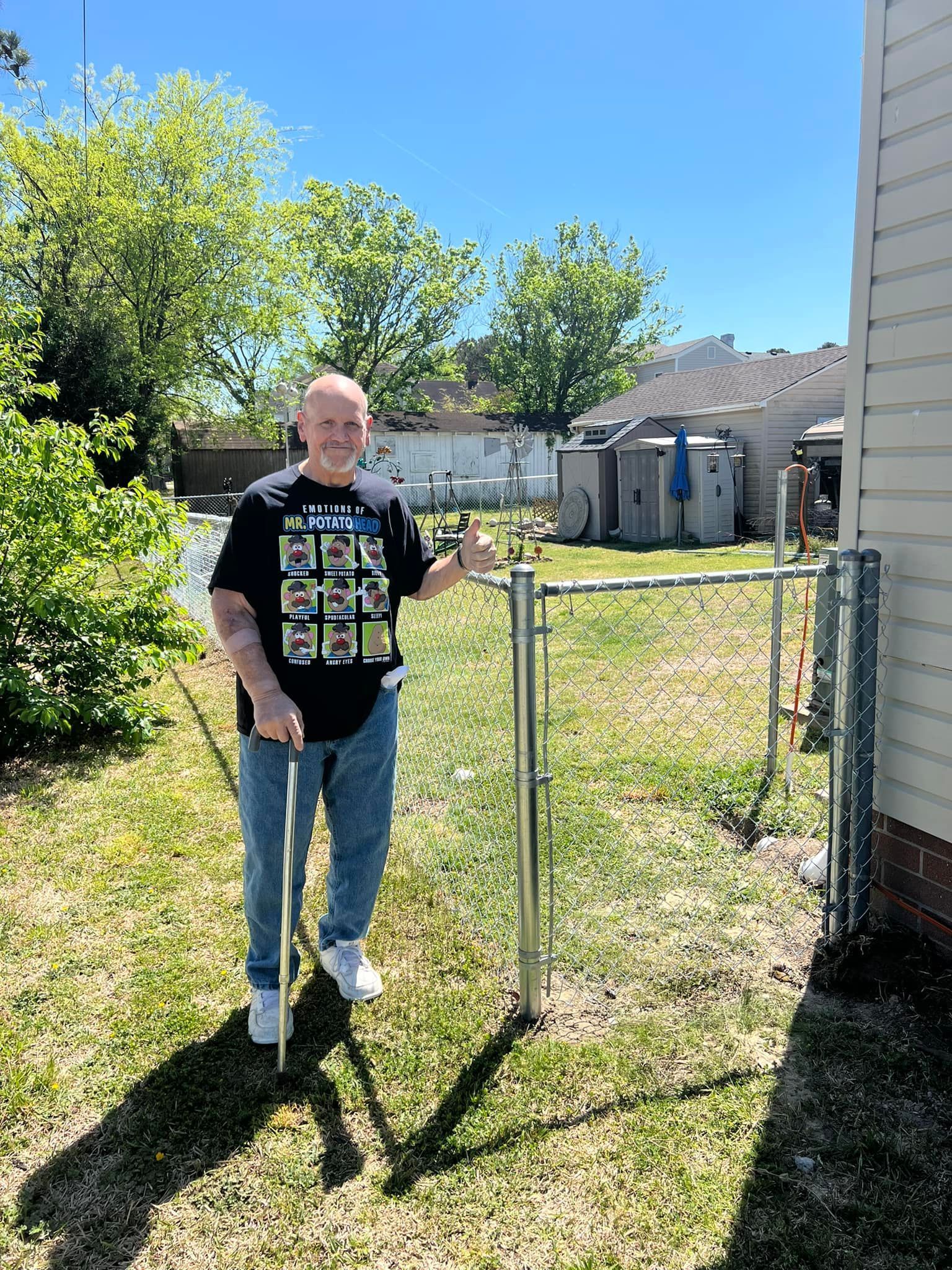 A man is standing next to a chain link fence in a backyard.
