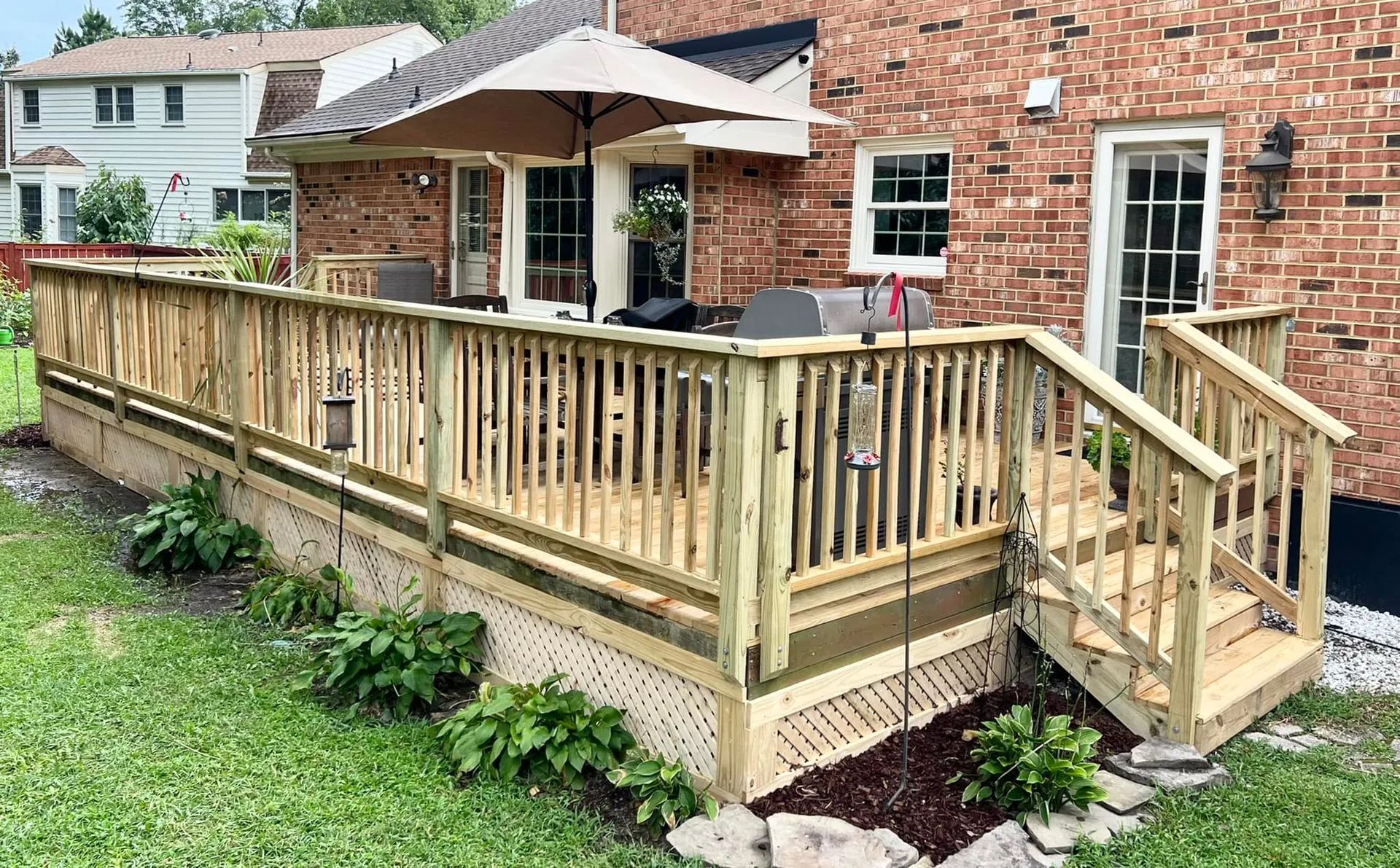 A wooden deck with stairs and umbrellas in front of a brick house.