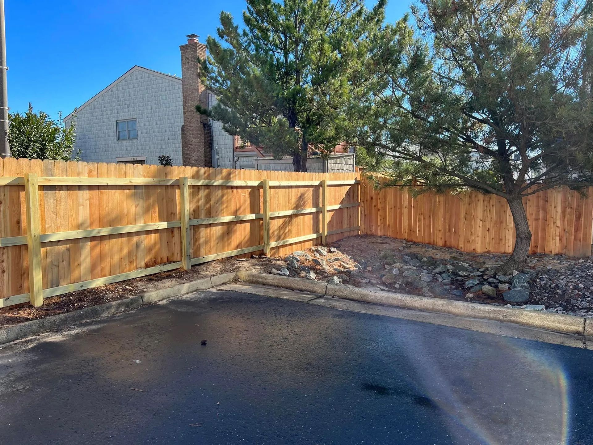 A wooden fence surrounds a parking lot in front of a house.