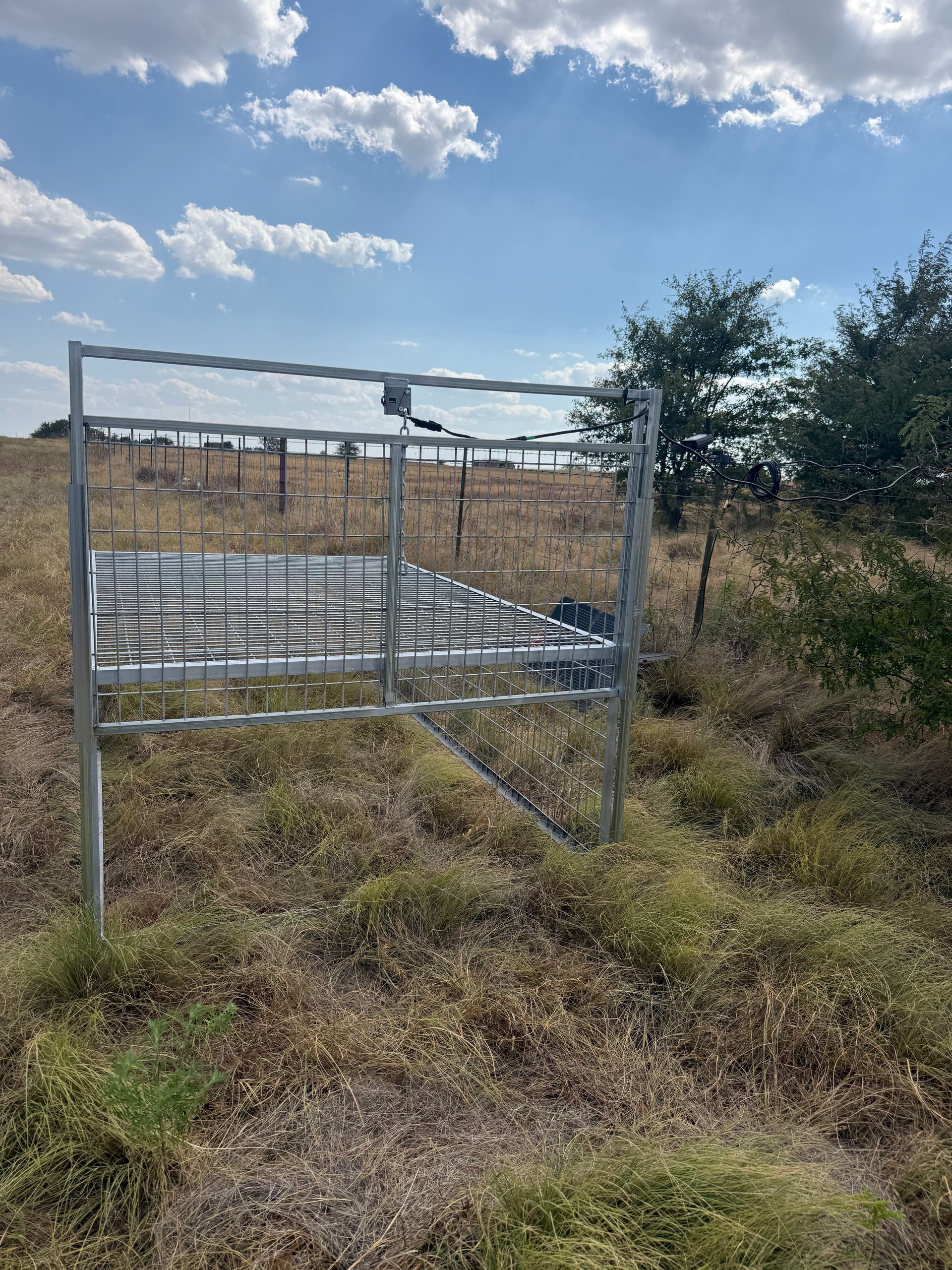 Cellular-controlled trap in a dry grassy field under a partly cloudy sky.