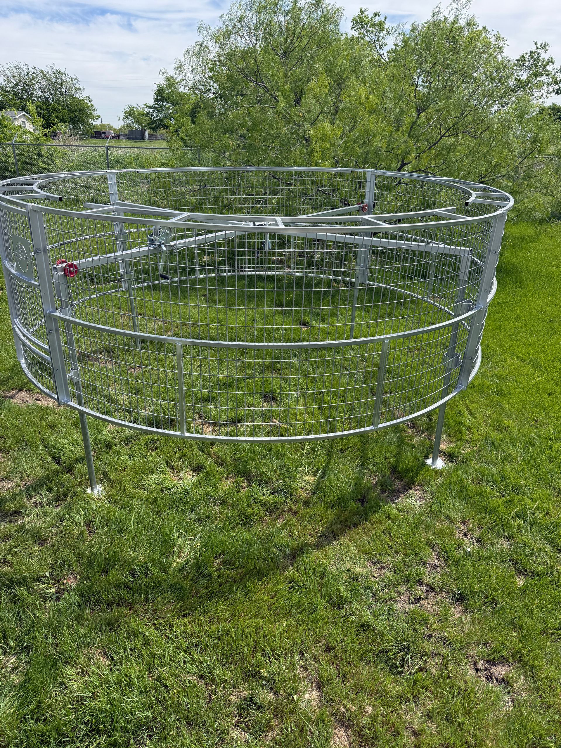 Large silver circular metal pen standing in a grassy yard with trees in the background