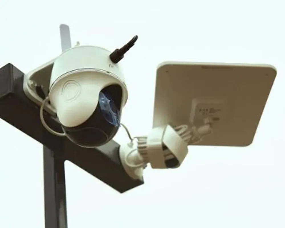 White security camera with a black lens, mounted with a solar panel on a black post.