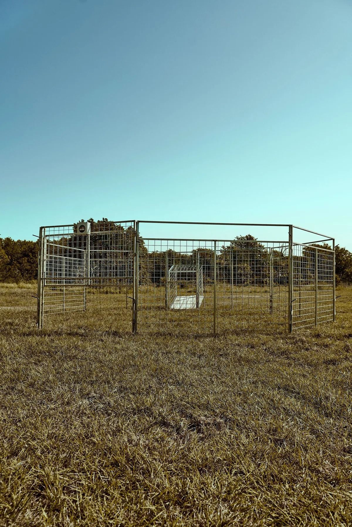 Metal structure in a field with trees in the background under a blue sky.