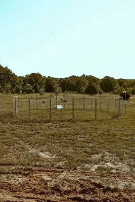 A fenced-in meteorological station in a field with trees in the background under a blue sky.