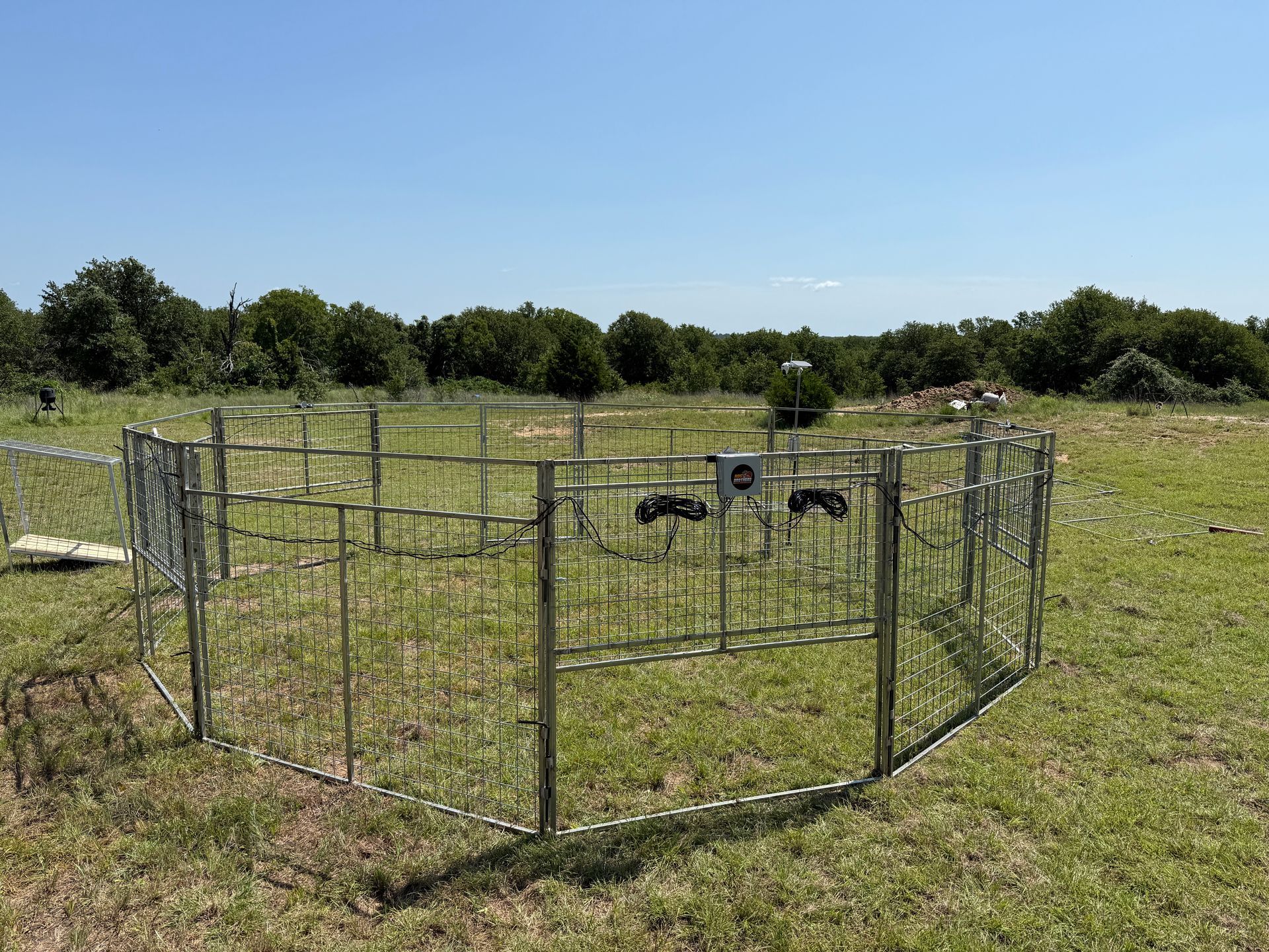 Small fenced livestock pen in a grassy field with goats under a clear blue sky
