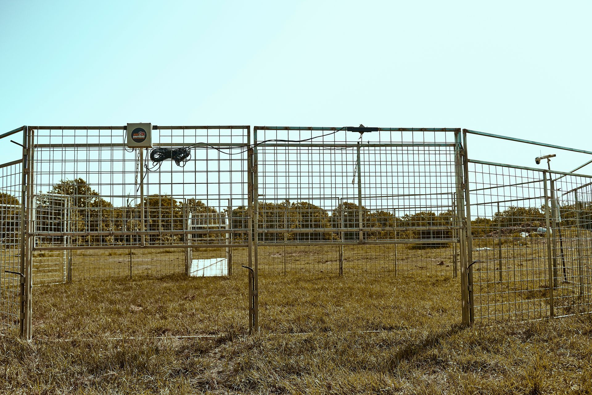 A fenced livestock pen in a dry field with hay and a small sign in front.