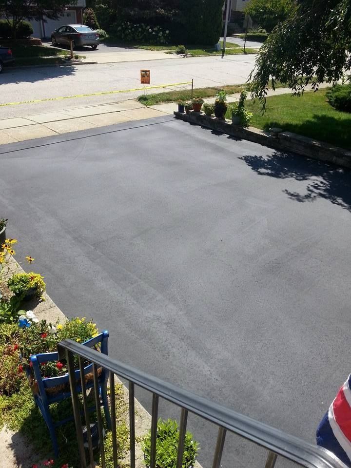 A freshly paved, dark asphalt driveway viewed from a porch, with a residential street in the background.
