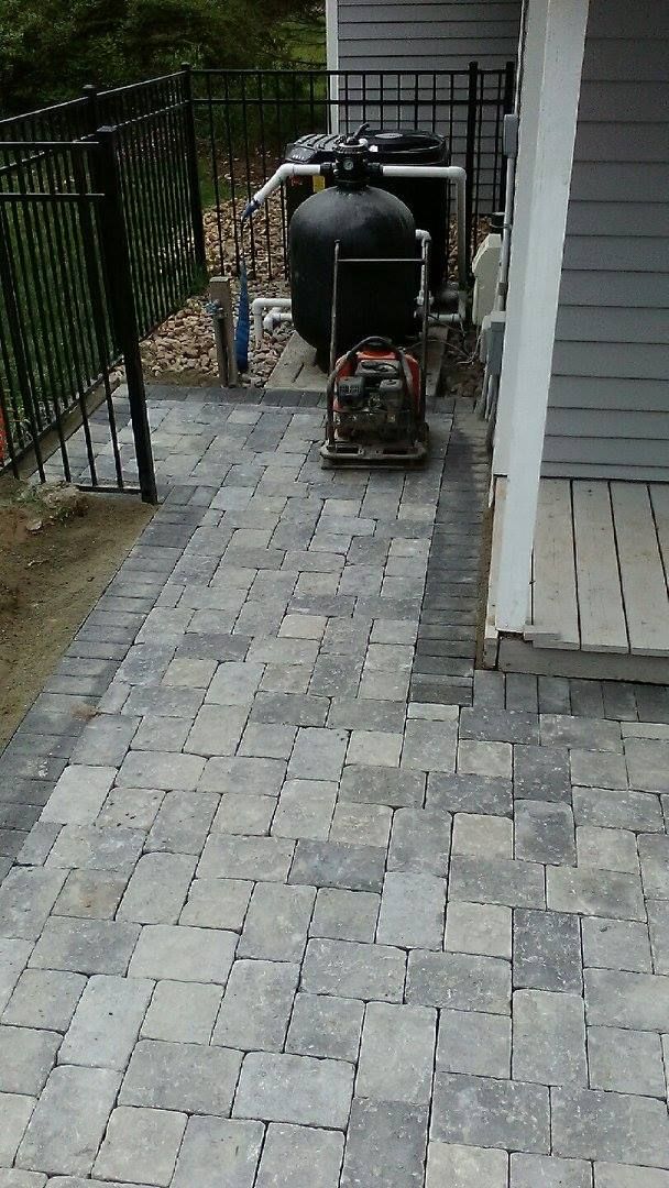 A gray paver walkway leading to a pool equipment area next to a house exterior.