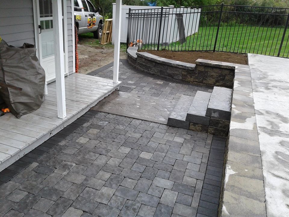 A stone paver patio featuring a small set of steps leading to a raised garden bed and a grey house exterior.