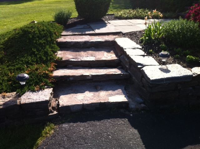 Natural stone steps with a matching side wall and low-voltage solar lights in a landscaped garden setting.