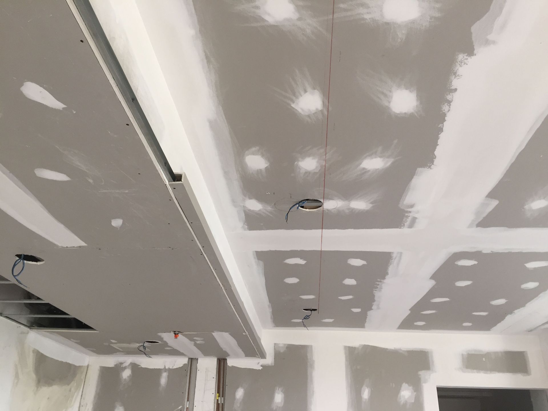 Ceiling under construction with gray drywall, white joint compound patches, and recessed light openings