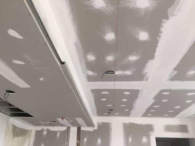 Ceiling under construction with gray drywall, white joint compound patches, and recessed light openings
