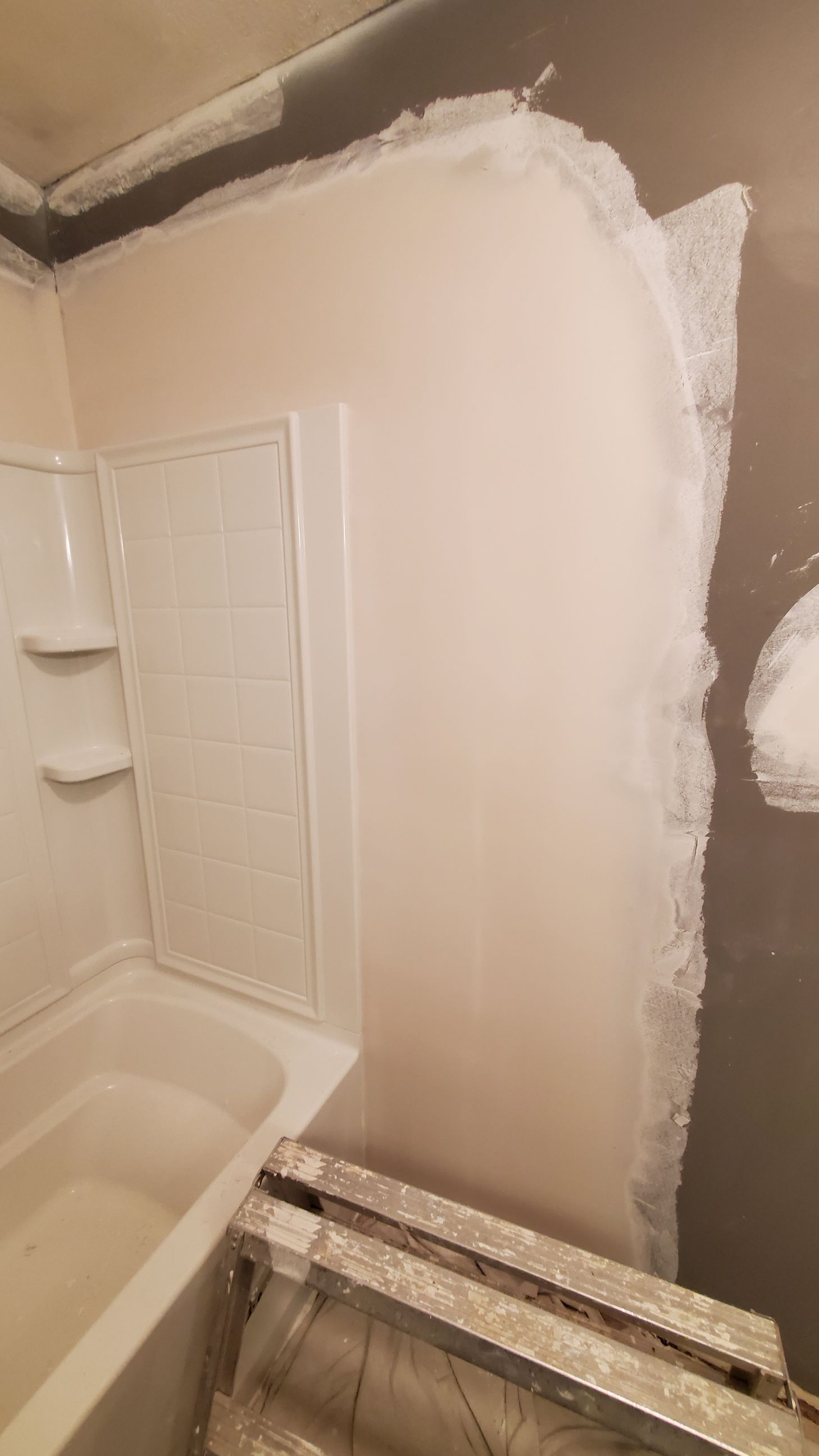 Bathroom wall partially patched with white drywall compound beside a tub and shower door