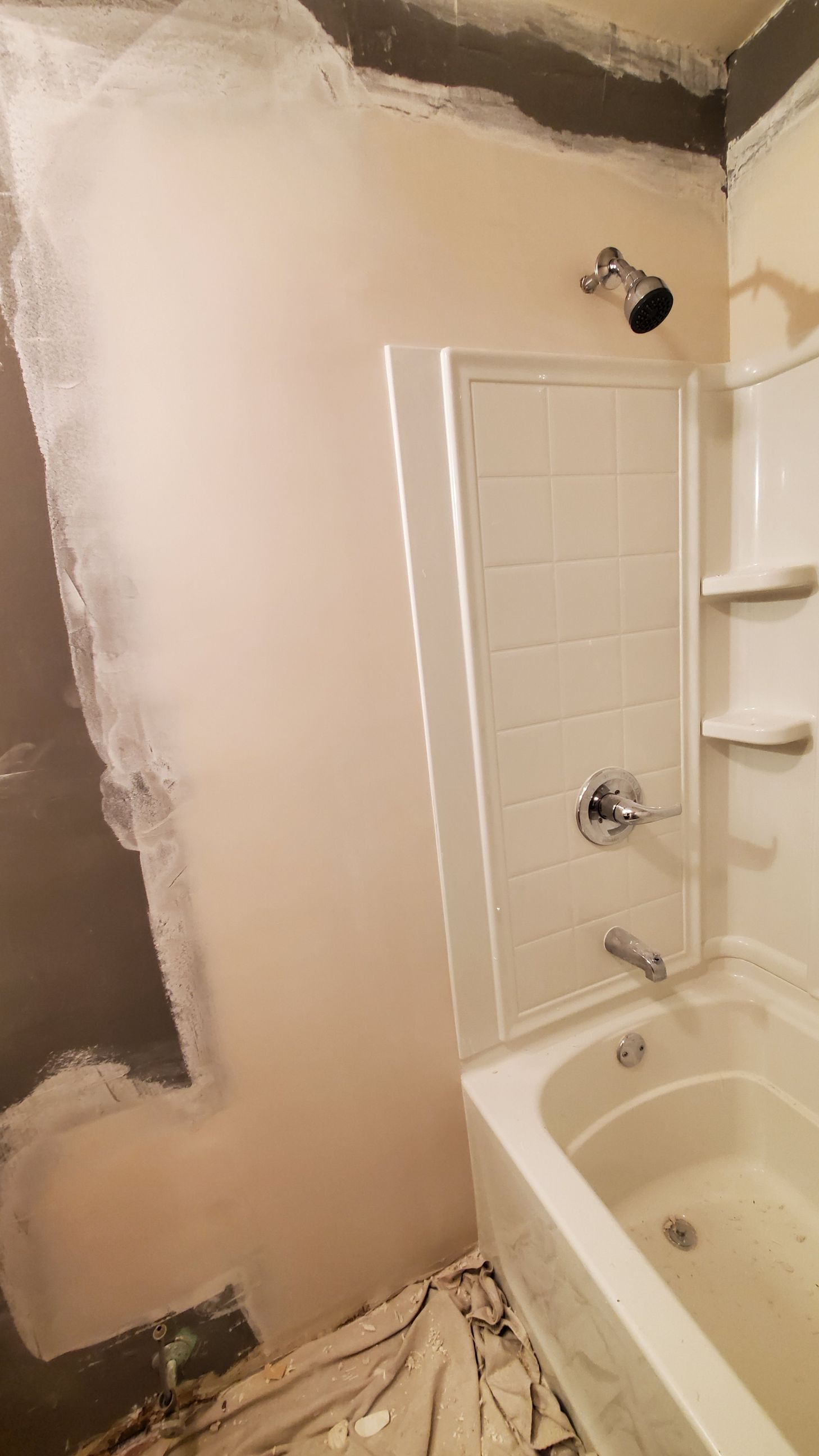 Bathroom shower stall with unfinished drywall, white tile, and tub surround.