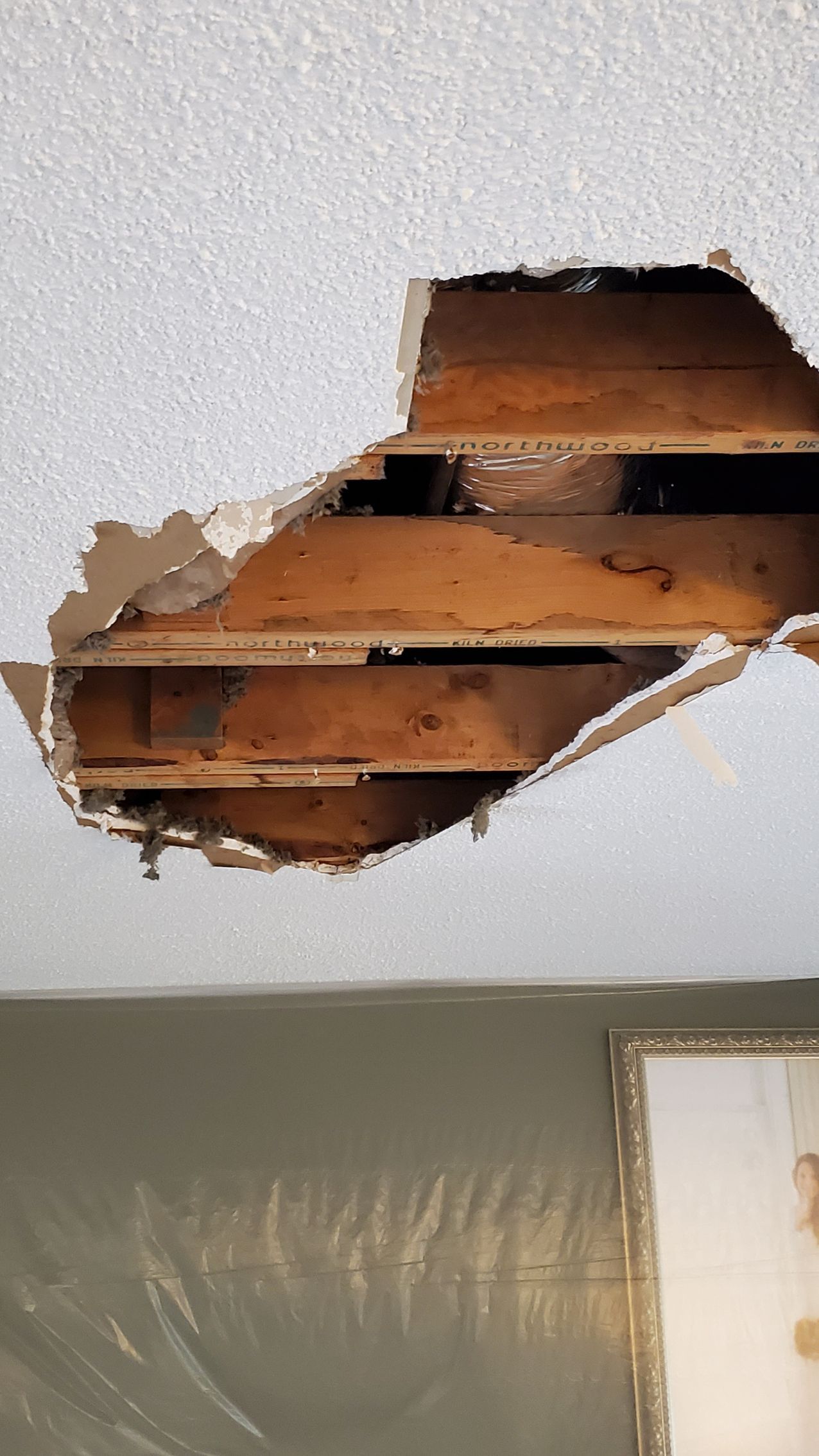 Ceiling hole exposing wooden beams and damage above a room wall