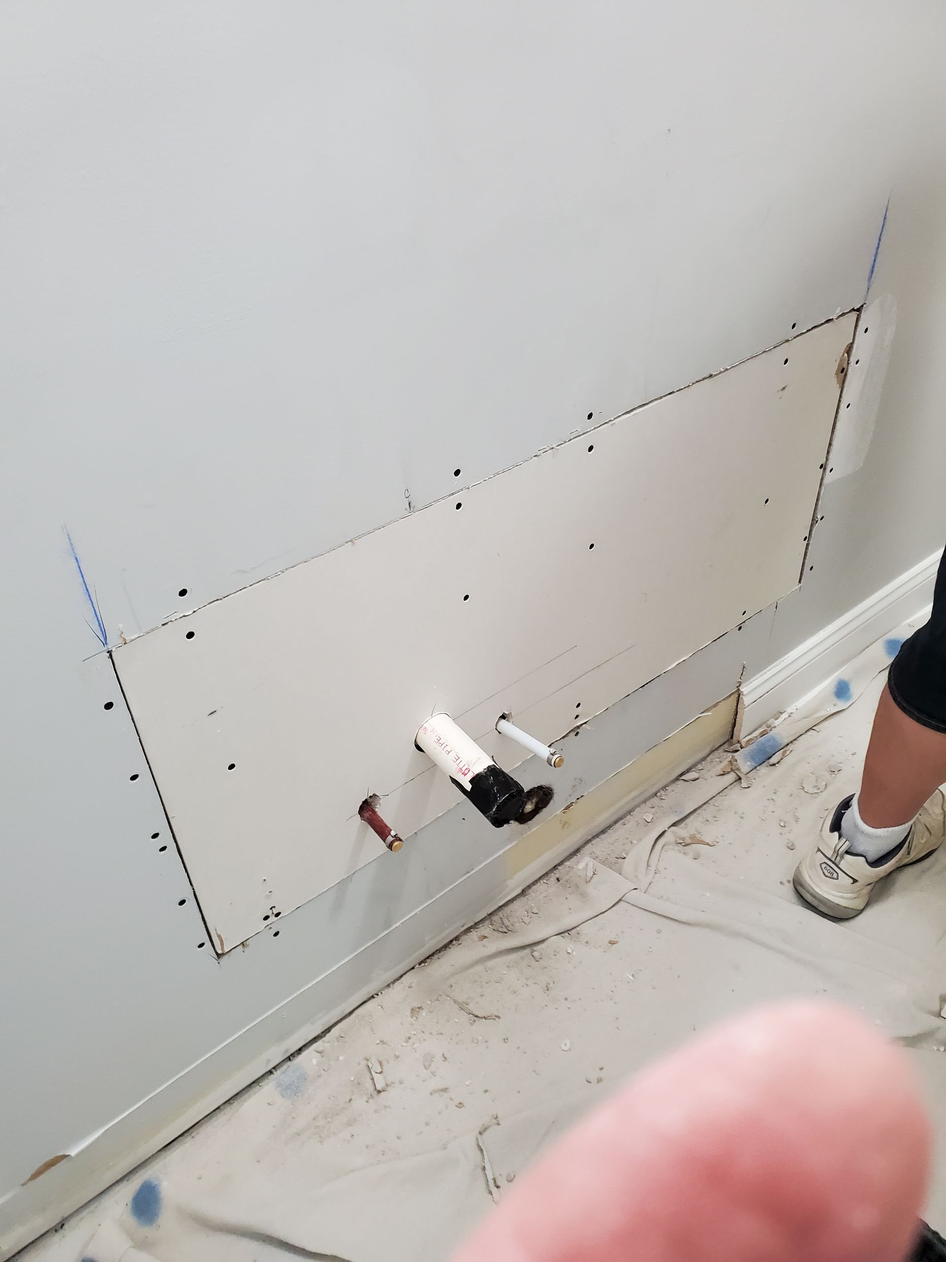 Wall cutout in a room under renovation, with tools on the floor and a person’s leg visible at right.