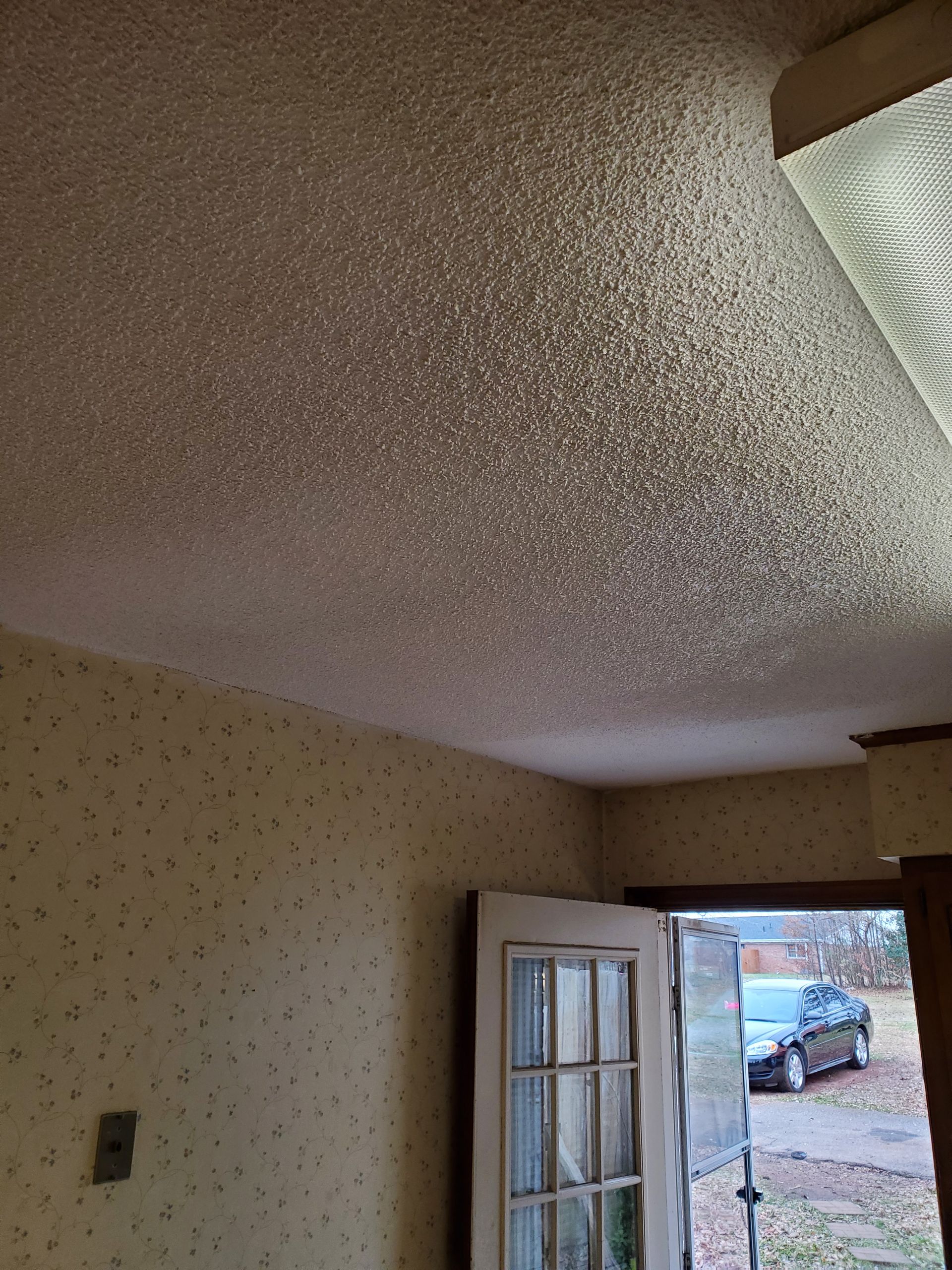 Textured white ceiling and open front door showing daylight and a parked car outside.