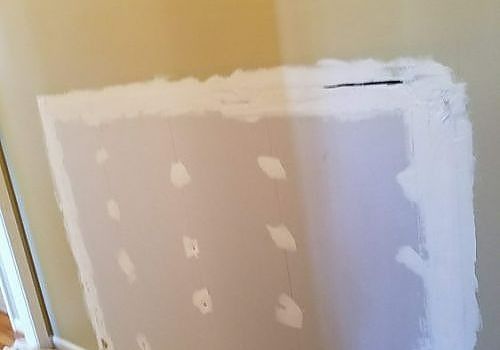 Partially patched drywall on a wall, with white joint compound spots and taped edges