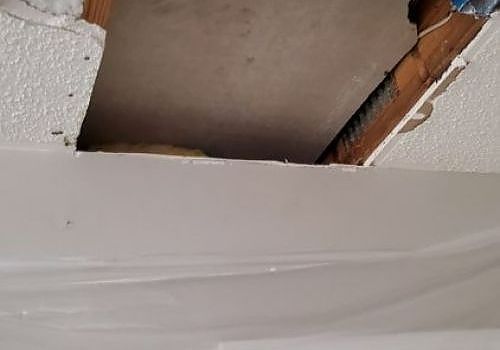Damaged ceiling with a large hole exposing wood and debris above a white surface