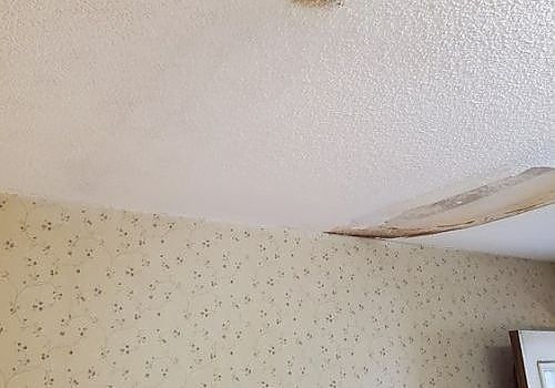 Water-damaged ceiling with a large peeled and sagging section above patterned wallpaper