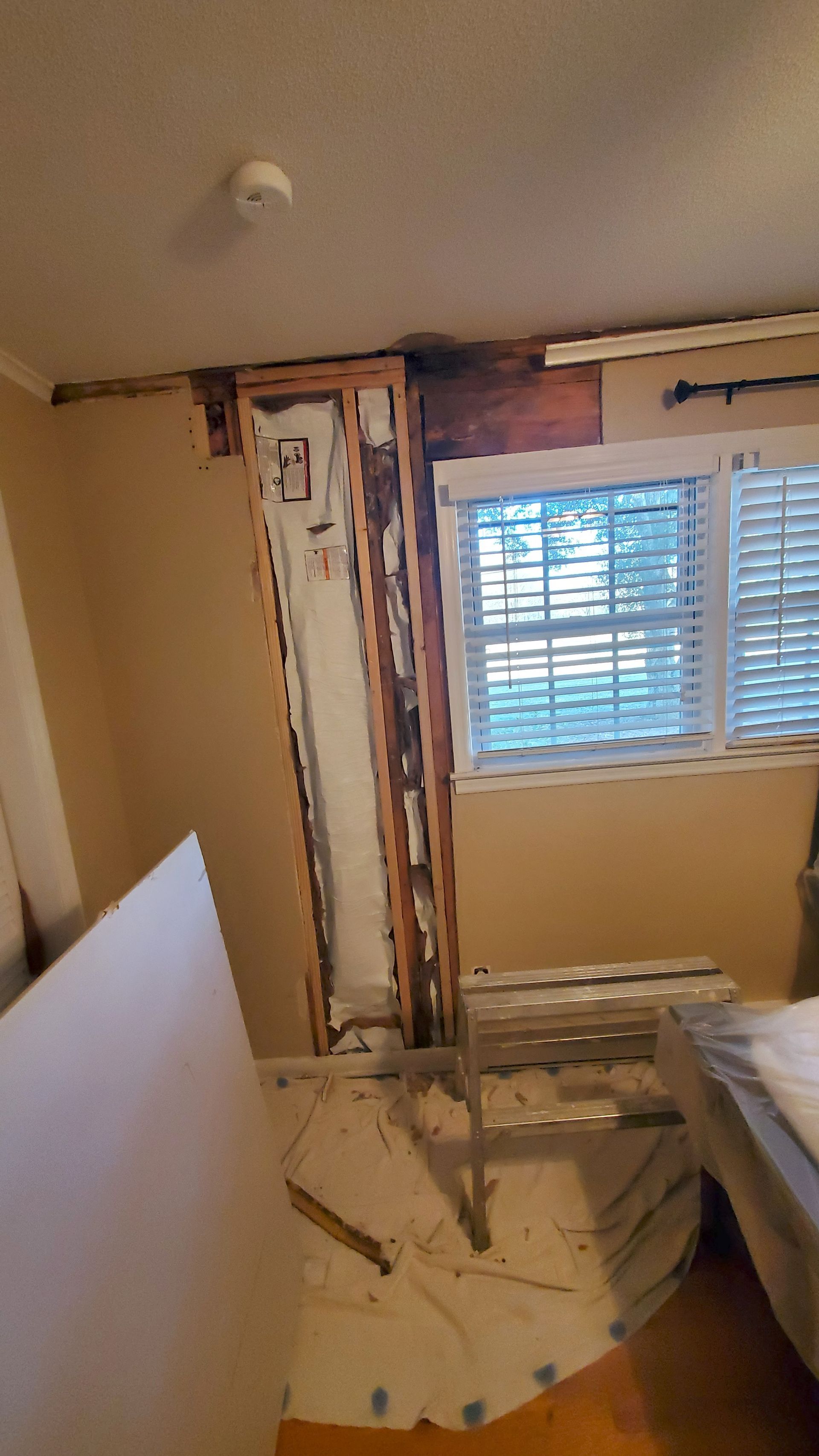 Partially demolished room with exposed wall framing, a window, and construction debris on the floor