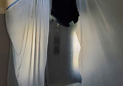White curtains parted to reveal a dim doorway with a hanging black garment above.