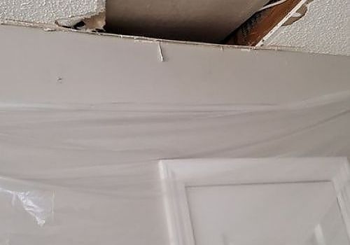 Damaged ceiling with a large hole and a door below, covered in plastic sheeting