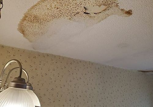 Water-stained ceiling with a large brown stain above a wall lamp.