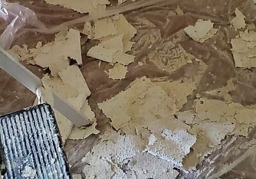 Kitchen floor covered with peeled-up linoleum and white debris during renovation