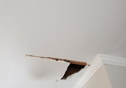 Damaged ceiling with a broken hole and loose plaster near the wall corner