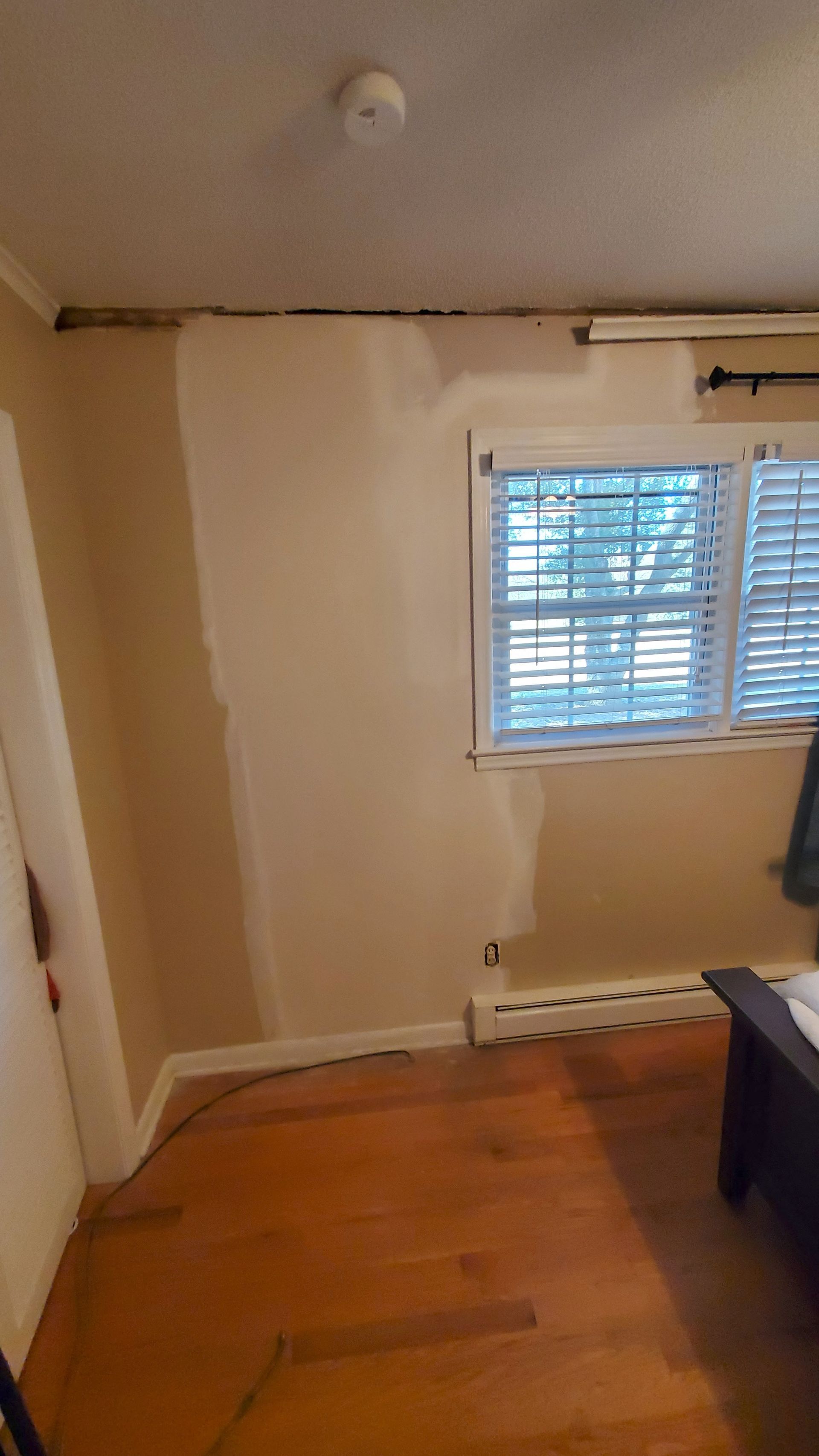 Empty beige room with wood floor, window blinds, and a desk edge on the right.