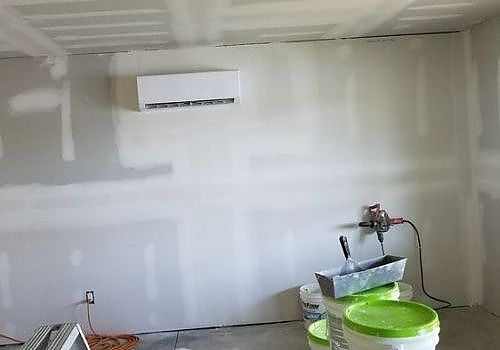 Partially finished room with white drywall, wall-mounted AC unit, and paint buckets on the floor