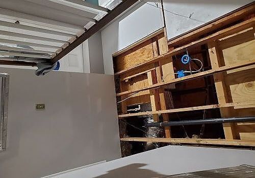 Partially demolished room with exposed wooden framing and a white wall under a metal roof